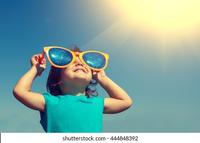 Happy little girl with big sunglasses  looking at the sun