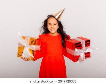 Happy little girl in a birthday cap is holding a big red gift box. holiday concept, place for text