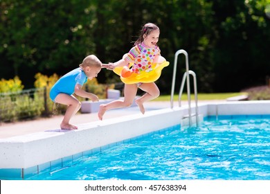 Happy Little Girl And Boy Holding Hands Jumping Into Outdoor Swimming Pool In A Tropical Resort During Family Summer Vacation. Kids Learning To Swim. Water Fun For Children.