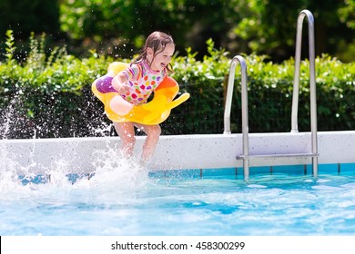 Happy Little Girl And Boy Holding Hands Jumping Into Outdoor Swimming Pool In A Tropical Resort During Family Summer Vacation. Kids Learning To Swim. Water Fun For Children.