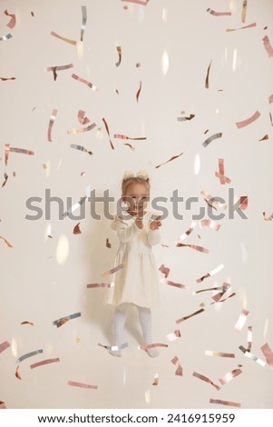 Happy little girl catches flying shiny confetti.