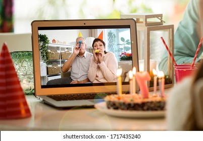Fröhliches kleines Mädchen, das zu Hause Geburtstag feiert, mit Eltern und großen Eltern auf Videoanruf. Laptop mit Seniorenpaar online, Kuchen mit Kerzen auf dem Tisch.