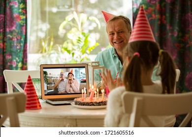 Happy little girl celebrating birthday at home with parents and grand parents on video call. Laptop with senior couple online, cake with candles on table. - Powered by Shutterstock