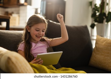 Happy little girl celebrating while playing games on digital tablet in the living room.  - Powered by Shutterstock