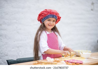 Happy little girl in an  chef costume helps to cook a pie by kneading the dough, a child smiles, cooking according to a recipe, a girl helps to cook for mom, a child's portrait and development.
