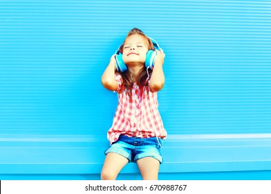 Happy Little Girl Child Listens To Music In Headphones On A Colorful Blue Background