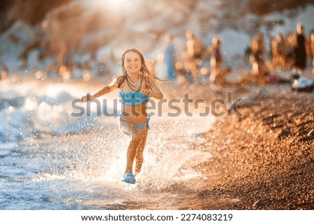 Happy little girl child runs on water along the shore splashing water. Golden backlight. Active recreation by sea.