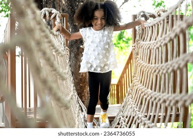 Happy little girl climbing on the Rope bridge in adventure park, having fun at playground   - Shutterstock ID 2364736055