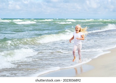 Happy Little Girl In Clothes On The Baltic Sea Beach On The Curonian Spit In Lithuania.