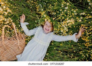 happy little girl in a cotton dress lies in a field of daisies in the summer at sunset. laughs, view from above - Powered by Shutterstock