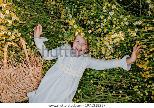 happy little\
girl in a cotton dress lies in a field of daisies in the summer at\
sunset. laughs, view from\
above