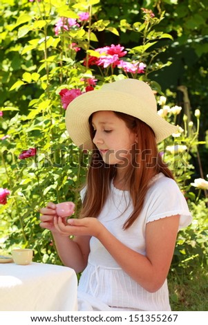 Happy little girl in cute hat playing with children's dishes in the tea party outdoors