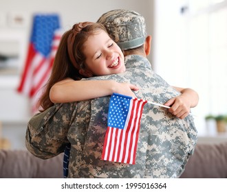 Happy little girl daughter with American flag hugging father in military uniform came back from US army, rear view of dad male soldier reunited  reunited with family at home