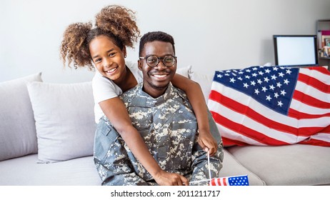 Happy little girl daughter with American flag hugging father in military uniform came back from US army, view of dad male soldier reunited reunited with family at home - Powered by Shutterstock