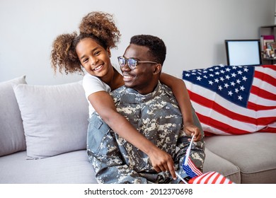 Happy little girl daughter with American flag hugging father in military uniform came back from US army, view of dad male soldier reunited reunited with family at home - Powered by Shutterstock