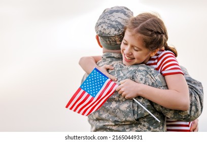 Happy little girl daughter with American flag hugging father in military uniform came back from US army, rear view of male soldier reunited with family while standing in green meadow on summer day - Powered by Shutterstock