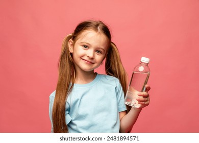 A happy little girl drinks water for health on a pink background. The child is holding a water bottle. A kid with a plastic bottle. Children's activity and energy, generation Z. body hydration concept - Powered by Shutterstock