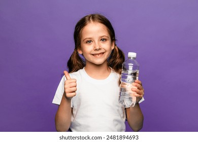 A happy little girl drinks water for health on purple background. The child is holding a water bottle. A kid with a plastic bottle. Children's activity and energy, generation Z. body hydration concept - Powered by Shutterstock