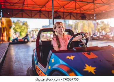 Happy little girl driving electric cars in amusement park