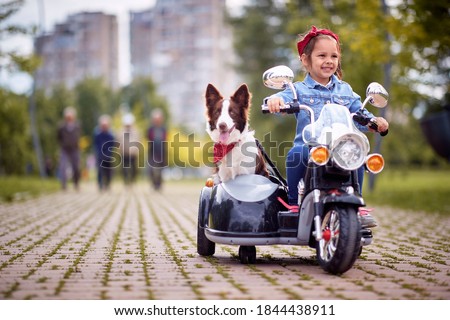 Happy little girl driving a toy motorcycle with her dog
