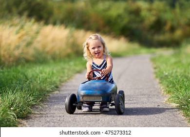 Happy Little Girl Driving Vintage Old Toy Car And Having Fun, Outdoors. Kid Leisure On Summer Day