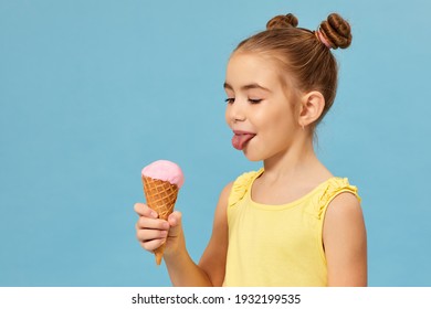 happy little girl eating ice cream in a waffle cone on blue background.