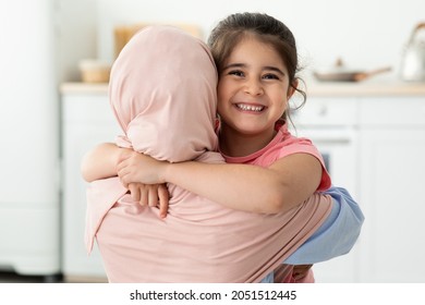 Happy Little Girl Embracing Her Muslim Mom In Hijab At Home, Adorable Female Child Hugging Islamic Mother And Smiling At Camera, Enjoying Spending Time With Mommy, Closeup Shot With Copy Space