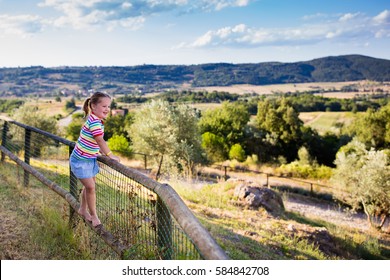 Happy Little Girl Enjoying Beautiful Valley And Mountains View Of Tuscany Landscape During Summer Vacation In Italy. Child Playing On Villa Terrace During Italian Holiday. Family Traveling In Toscana