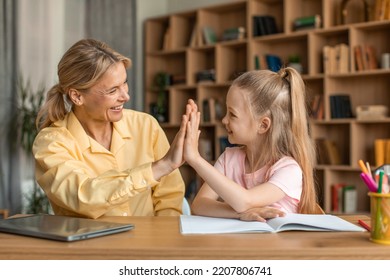 Happy Little Girl Giving Her Female Teacher High Five, Cheerful Woman And Child Preschooler Sitting At Table Together, Learning Alphabet And Drawing, Celebrating Success