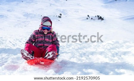 Happy little girl going down the hill on sleigh in the mountain resort