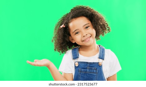 Happy, little girl and green screen with smile for product placement isolated against a studio background. Portrait of cute female kid smiling with palm of open hand showing advertisement on mockup