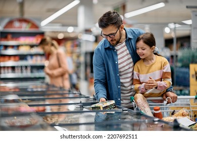 Happy little girl and her dad choosing food at refrigerated section while shopping in supermarket. - Powered by Shutterstock