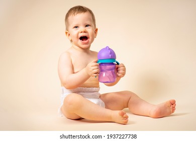 Happy Little Girl Holding Baby Food In A Bottle With Water In Her Hands, Smiling. Child In A Diaper Toddler On A Solid Background Monochromatic In The Studio Shows Emotions