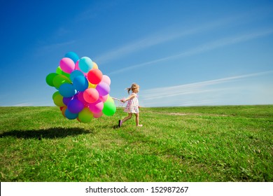 Happy little girl holding colorful balloons. Child playing on a green meadow. Smiling kid.
