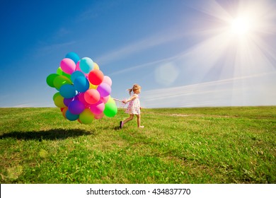 Happy little girl holding colorful balloons. Child playing on a green meadow. Smiling kid. 