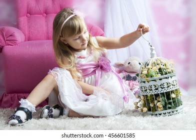 Happy Little Girl Holding Decorative Bird Cage Full Of Flowers. Studio Shot In Provence Style Interior