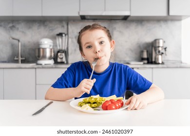 Happy little girl holding a fork in her mouth. A pre-teenage girl has breakfast in the kitchen at home with a plate of waffles, vegetables and cheese. Selected focus. High quality photo. - Powered by Shutterstock