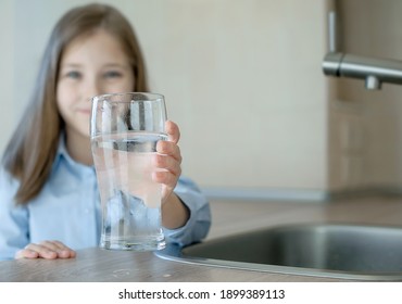 Happy little girl holding a glass of water. Selective focus on child hand with glass of water in foreground. Hydration. Water quality check. World water monitoring day. Environmental pollution problem