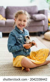 happy little girl is holding a young fluffy guinea pig in her arms, stroking it and hugging it. A pet, a rodent, her friend. Pet care. Training in responsibility and care of an animal.