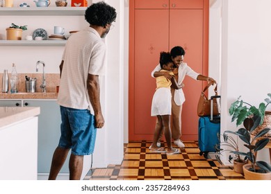 Happy little girl hugging her mom as she comes in through the doorway with her travel bags. Parent and child reuniting in their welcoming home, greeting with excitement after returning from a trip. - Powered by Shutterstock