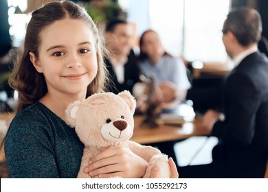 Happy Little Girl Is Hugging Teddy Bear At Office Of Family Lawyer. Registration Of Guardianship. Family In Office Of Family Lawyer.