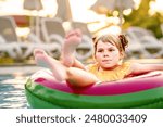 Happy little girl with inflatable toy ring float in swimming pool. Little preschool child learning to swim and dive in outdoor pool of hotel resort. Healthy sport activity and fun for children.