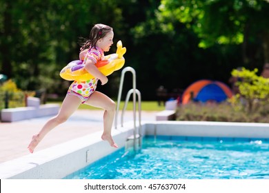 Happy Little Girl With Inflatable Toy Ring Jumping Into Outdoor Swimming Pool In A Tropical Resort During Family Summer Vacation. Kids Learning To Swim. Water Fun For Children.