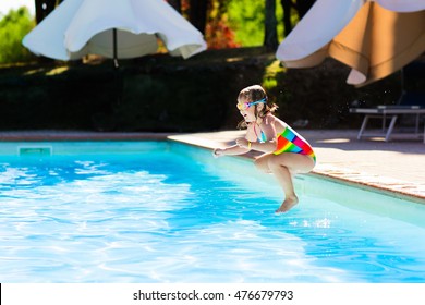 Happy Little Girl With Inflatable Toy Ring Jumping Into Outdoor Swimming Pool In A Tropical Resort During Family Summer Vacation. Kids Learning To Swim. Water Fun For Children.