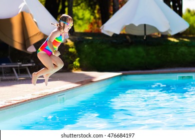 Happy Little Girl With Inflatable Toy Ring Jumping Into Outdoor Swimming Pool In A Tropical Resort During Family Summer Vacation. Kids Learning To Swim. Water Fun For Children.