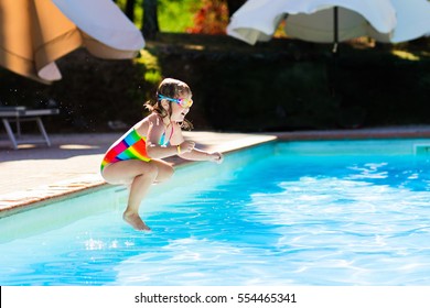 Happy Little Girl With Inflatable Toy Ring Jumping Into Outdoor Swimming Pool In A Tropical Resort During Family Summer Vacation. Kids Learning To Swim. Water Fun For Children