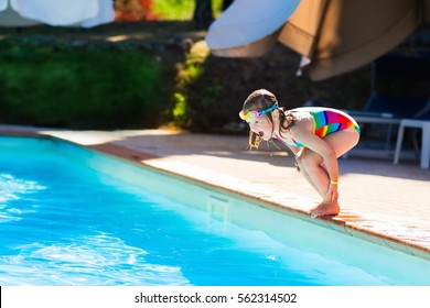 Happy Little Girl With Inflatable Toy Ring Jumping Into Outdoor Swimming Pool In A Tropical Resort During Family Summer Vacation. Kids Learning To Swim. Water Fun For Children