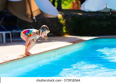 Happy Little Girl With Inflatable Toy Ring Jumping Into Outdoor Swimming Pool In A Tropical Resort During Family Summer Vacation. Kids Learning To Swim. Water Fun For Children