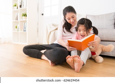 happy little girl laugh holding teddy bear watching new story book to see special content was pleasantly surprised with the beautiful mom sitting together on floor enjoy holiday afternoon time.