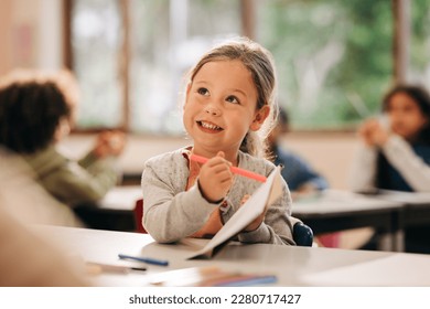 Happy little girl learning to draw with a colour pencil in an elementary art class. Primary school kid talking to her teacher as she receives quality education in a positive learning environment. - Shutterstock ID 2280717427